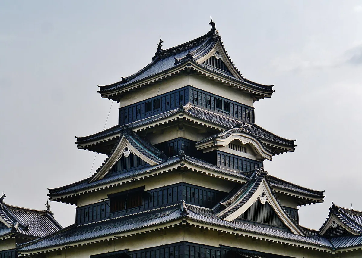 松本城の大天守の上部。黒い壁と白い漆喰、何重にも重なる屋根が曇り空を背に立っている