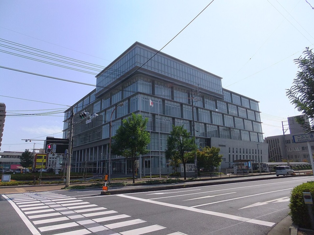 岩国市役所の本庁舎。ガラス張りで6階建てほどの四角い建物を、横断歩道のある交差点から見ている