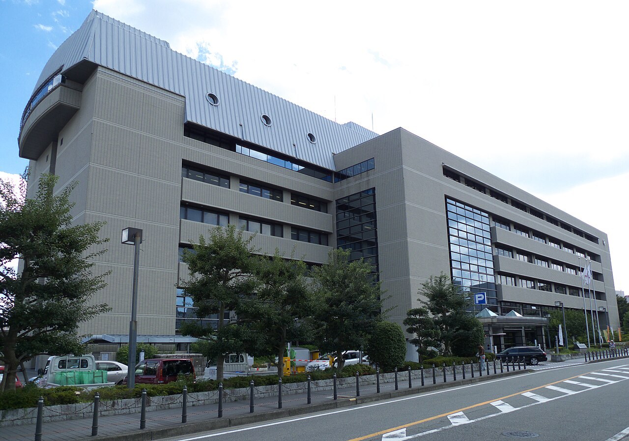 川西市役所の庁舎。灰色の大きな建物で、前に車道がある