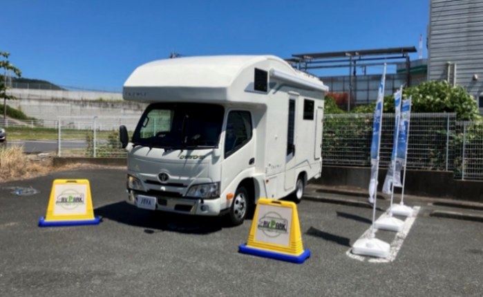 コンビニの駐車場に停めたキャンピングカーと、RVパークの置き看板2つ