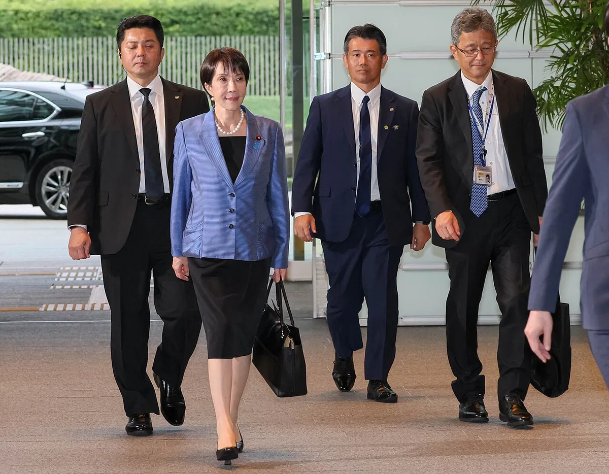 青いジャケットの高市首相が、職員らと並んで首相官邸の玄関ホールを歩いている