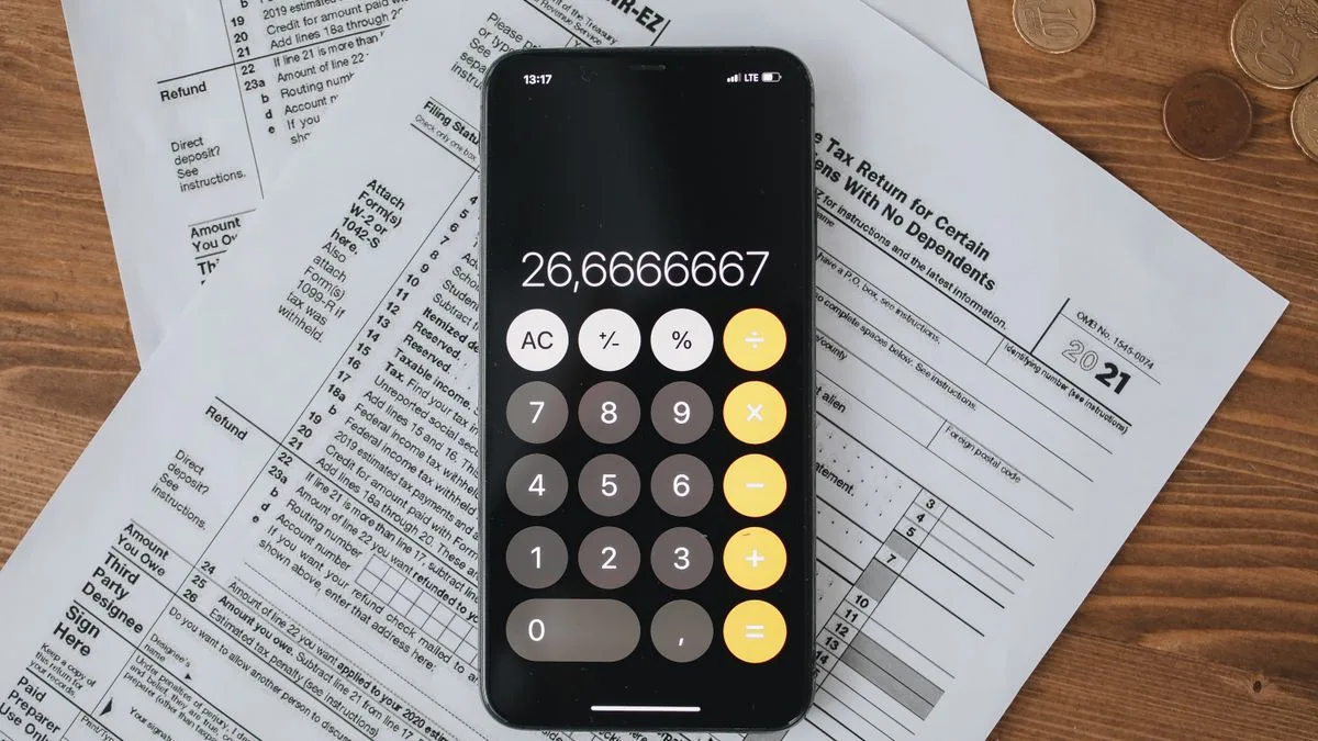 木の机に置かれた書類の上で、スマートフォンの電卓に数字が表示されている