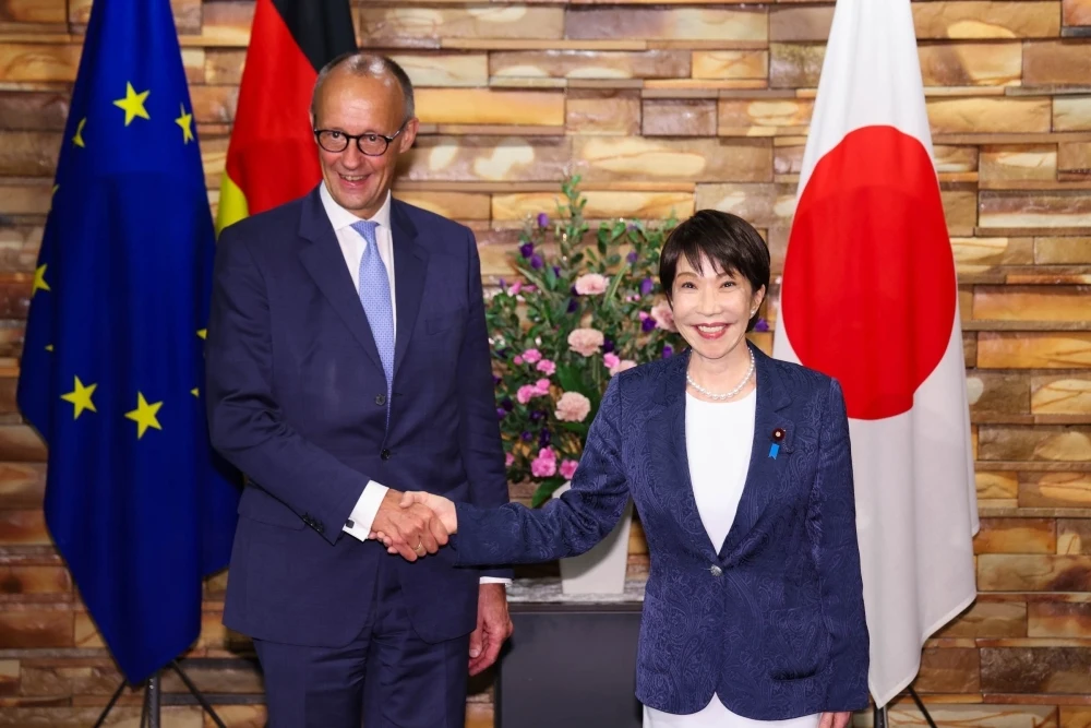 日独両国の国旗の前で握手する高市首相とメルツ首相