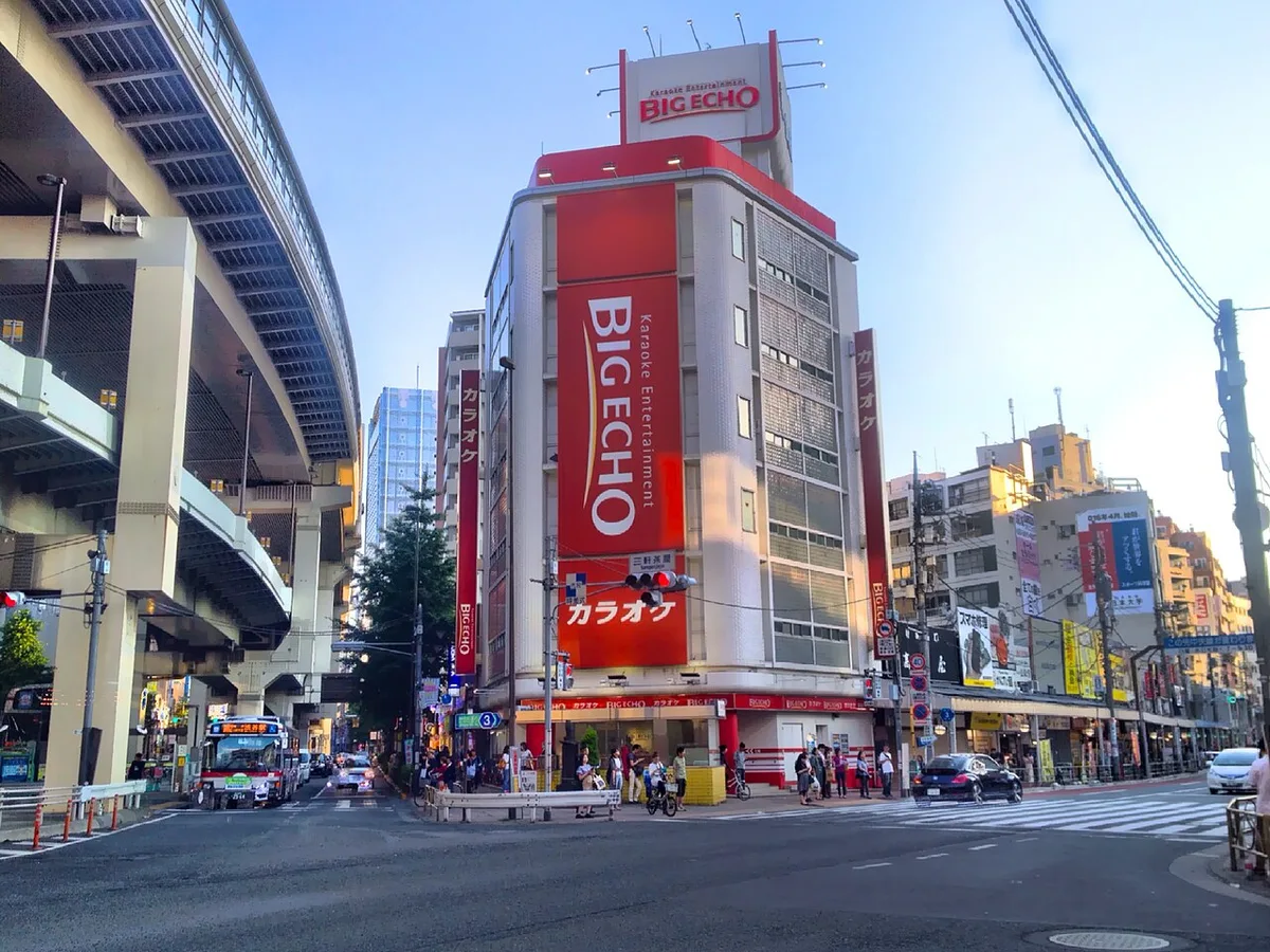 三軒茶屋交差点。首都高速の高架の下を道路が通り、角にカラオケ店のビルが建っている
