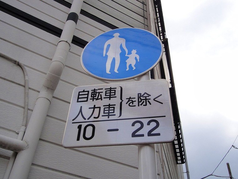 浅草の通りに立つ道路標識「歩行者専用」(325の4)。青い丸に白い大人と子どもの絵で、下の補助標識に「自転車・人力車を除く」「10-22」とある。10時から22時まで車は通れないが、自転車と人力車は除外されている(2012年撮影)