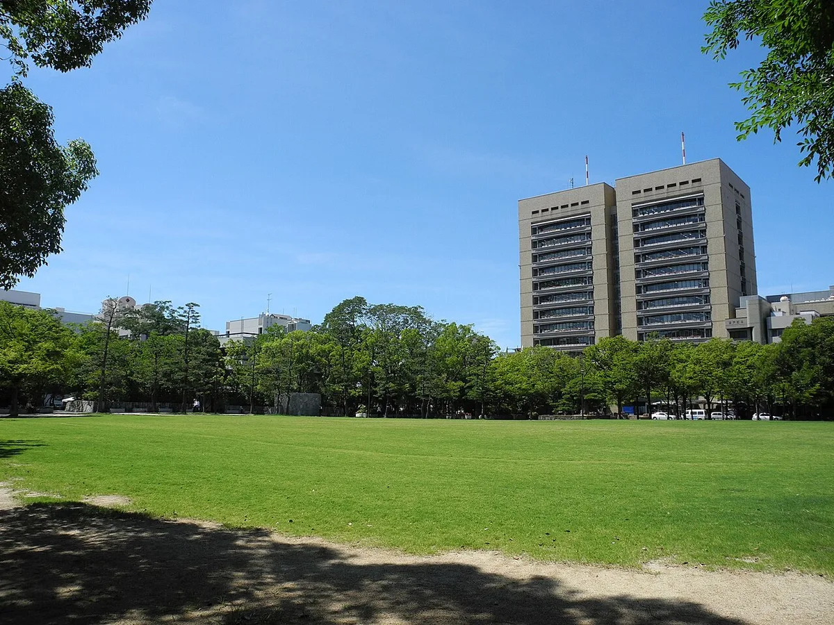 高松市中央公園の芝生の広場。木立の向こうに高松市役所の高い庁舎が見える