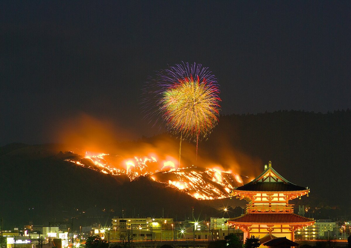 若草山焼き。夜の若草山の斜面に炎が広がり、上空に花火が開く。手前に平城宮跡の朱雀門