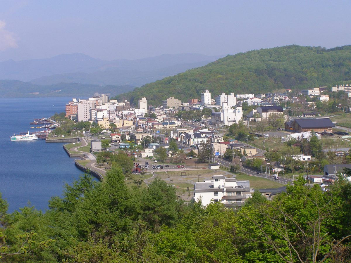 高台から見た洞爺湖温泉の街並み。湖岸にホテルや旅館が並び、背後に緑の山がある